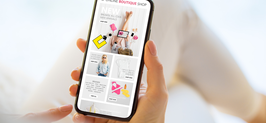 A hand holding a smartphone displaying an online boutique shop interface, featuring new arrivals, trendy fashion items, and popular brands. The screen is vibrant with images of clothing, accessories, and promotional banners.